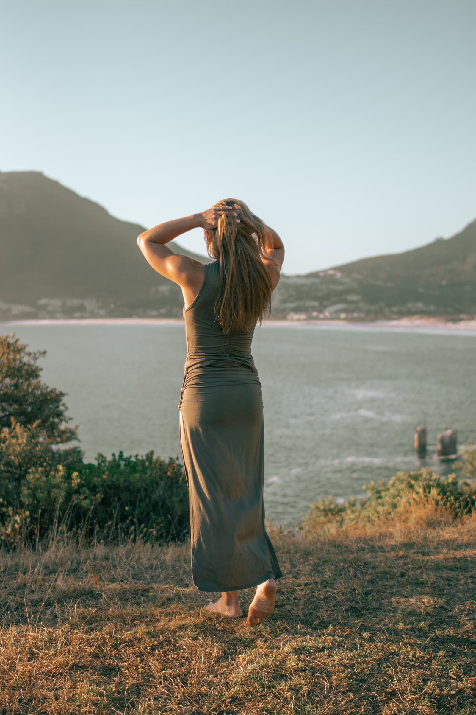Madison outdoors with arms raised, back to camera, overlooking the water
