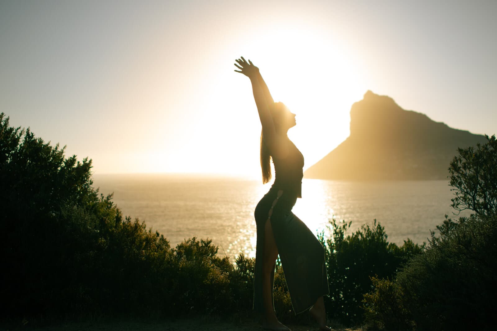 Silhouette of a woman with arm raised at sunset by the ocean